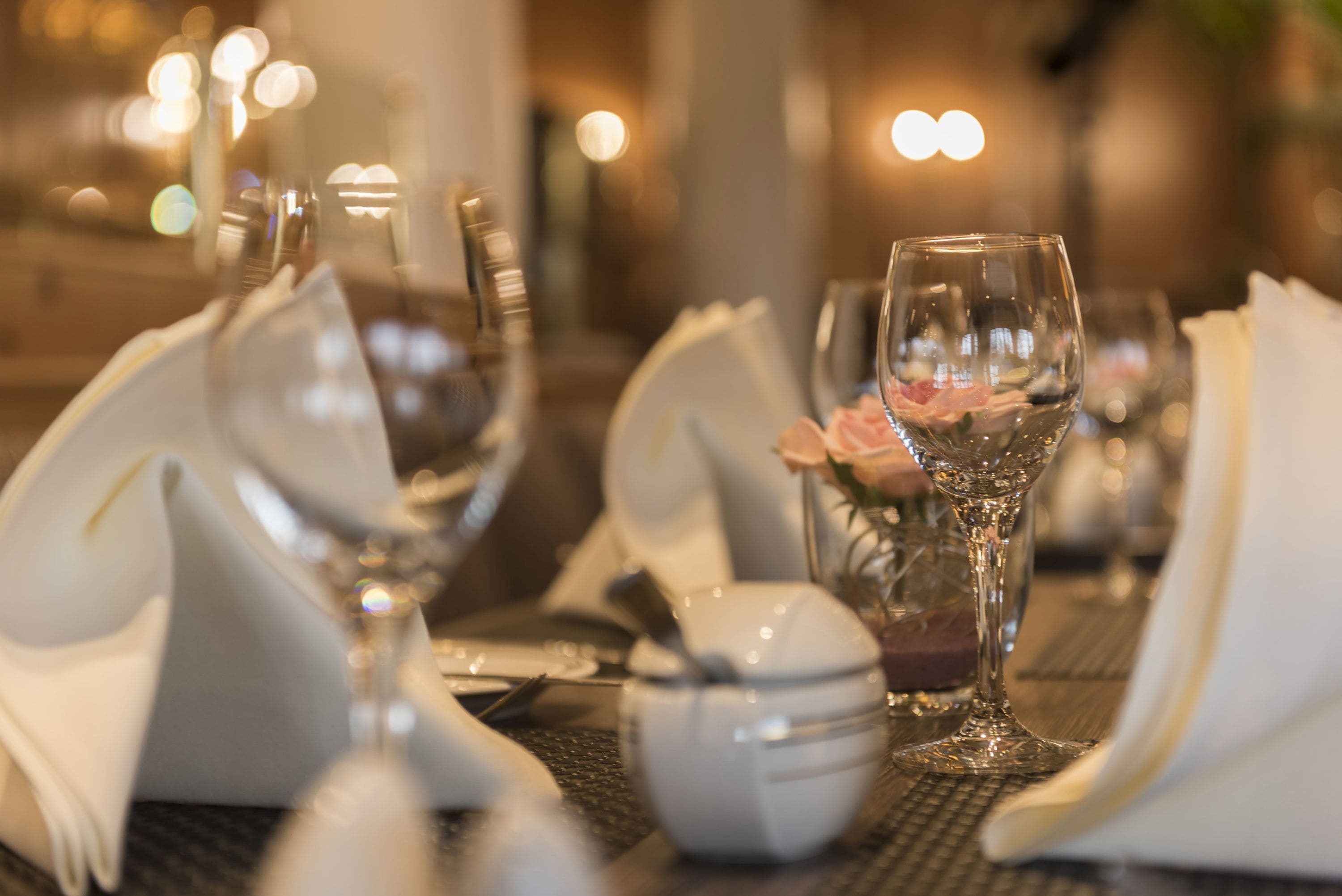 A dining table set with white napkins, a glass, a small bowl, and a glass of water.