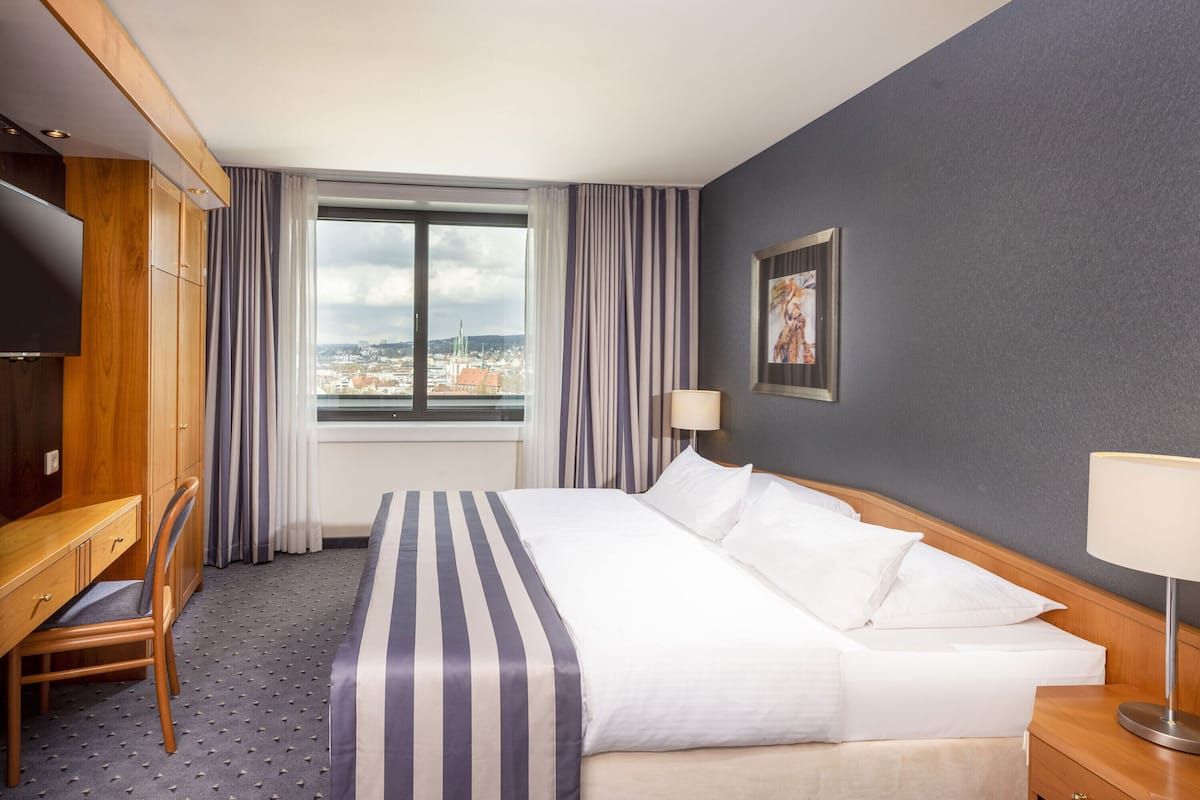 A hotel room with a large bed, a desk, a chair, a TV, and a window with curtains.