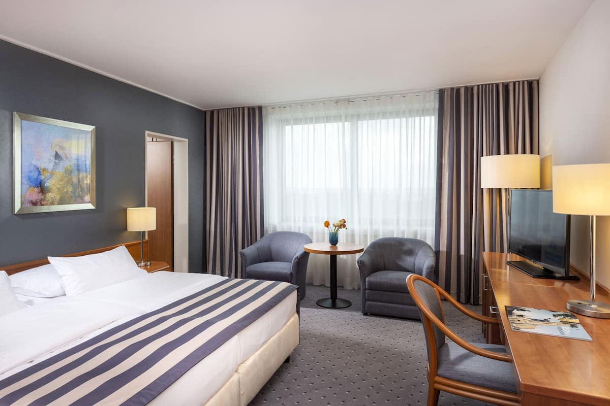 A hotel room with a large bed, two armchairs, a small table, and a TV.