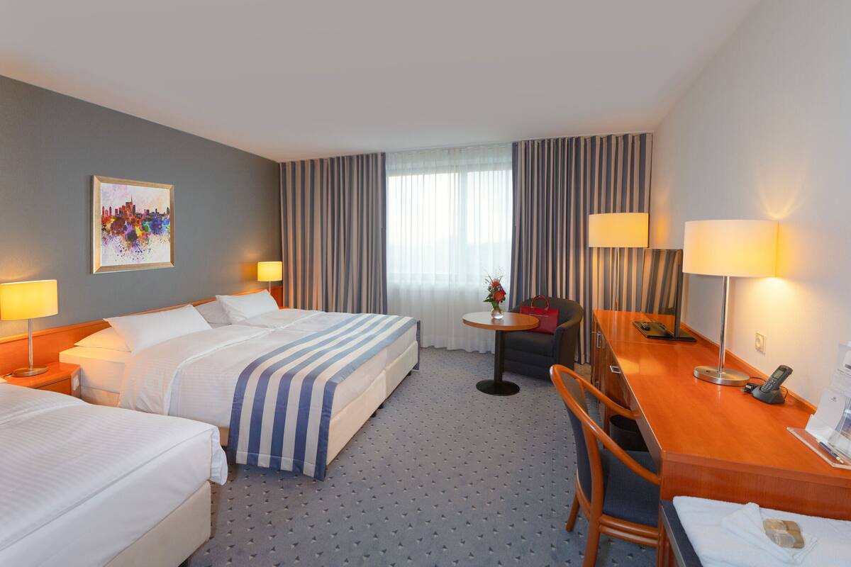 A hotel room with two beds, a desk, a chair, a small table, and a window with curtains.