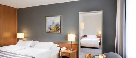 Habitación de hotel con una cama grande, mesitas de noche, una silla, una pequeña mesa con flores y un cuadro en la pared.