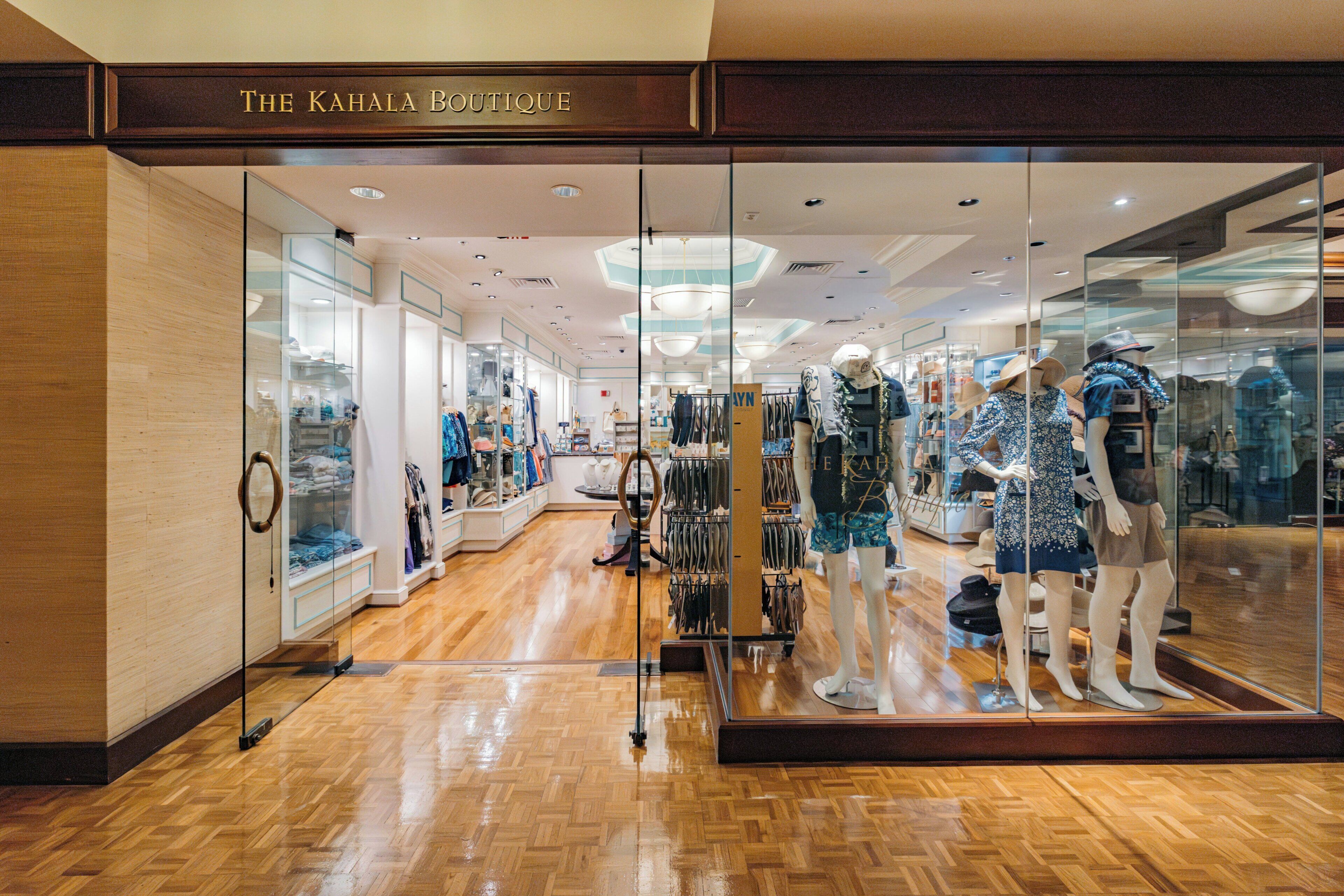 A boutique store with mannequins displaying clothing, wooden flooring, and glass display cases.