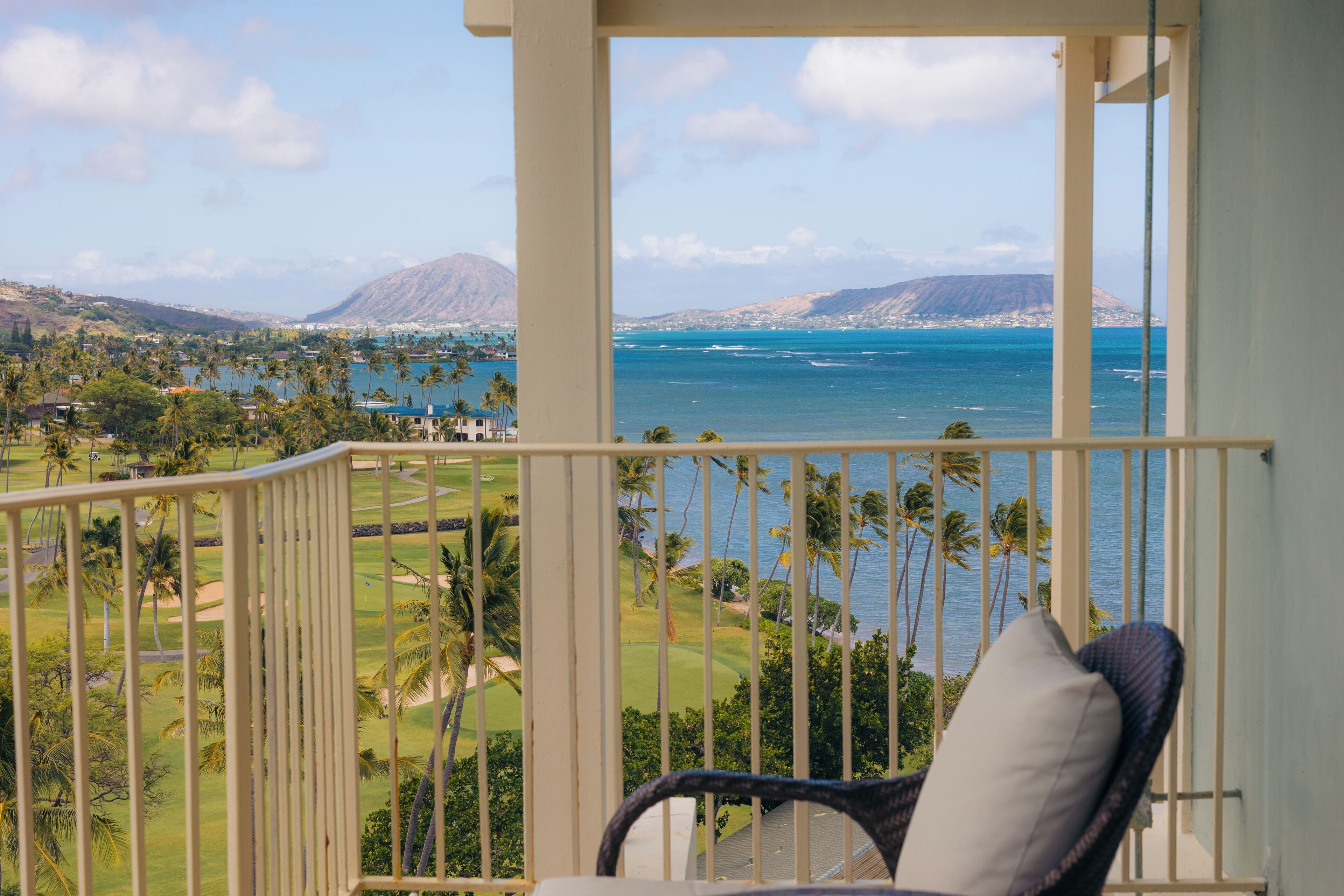 A balcony with a view of a golf course and the ocean.