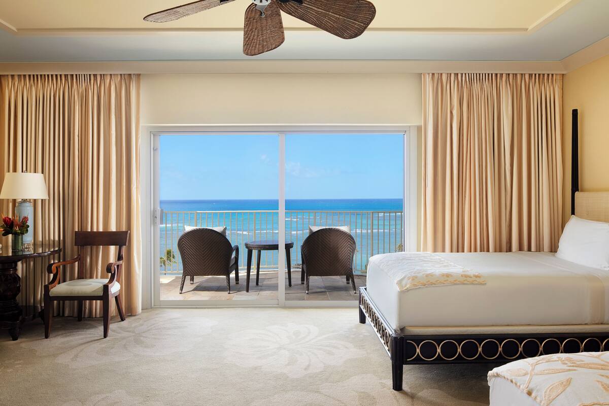 A hotel room with a bed, a desk, a chair, and a view of the ocean through a sliding door.