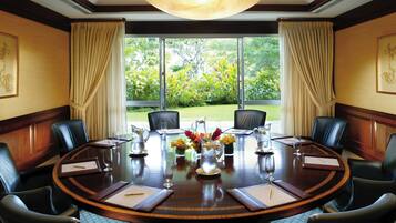 A conference room with a round table, black leather chairs, a large window with curtains, and a chandelier.
