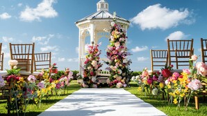 A gazebo with a white exterior and a dome roof, surrounded by a floral arrangement and wooden chairs.
