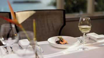 A dining table with a plate of food, a glass of white wine, and dining utensils.