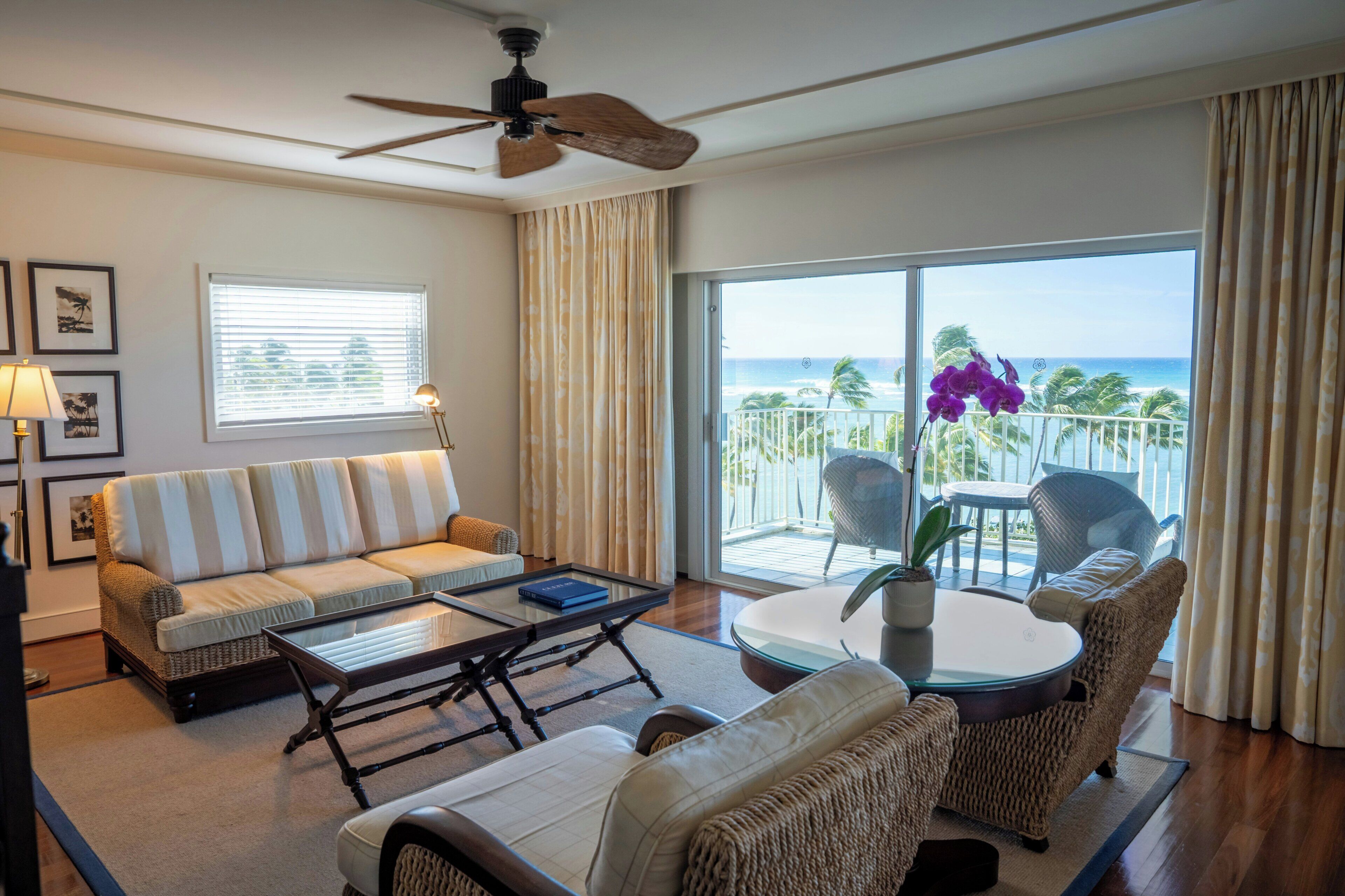 A hotel room with a balcony, a sofa, a coffee table, and a dining table with chairs.