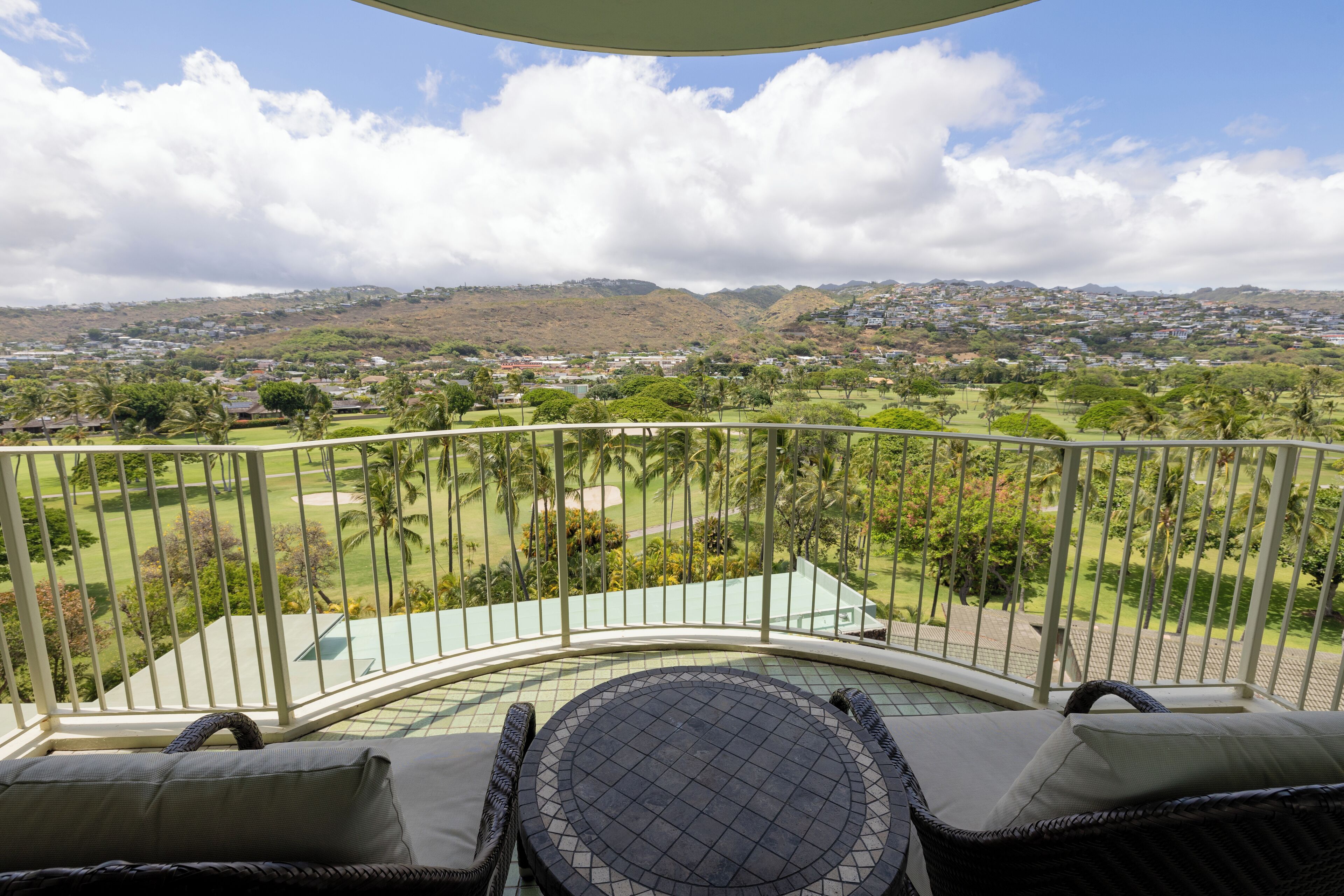 Un balcon agrémenté de meubles en osier, avec vue sur un terrain de golf et sur des collines lointaines.