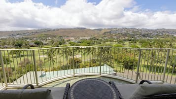A balcony with wicker furniture, a view of a golf course, and distant hills.