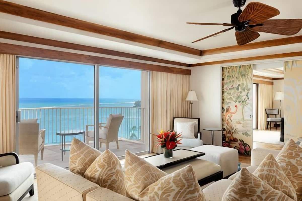 A spacious living room with a large balcony, a ceiling fan, and a view of the ocean.
