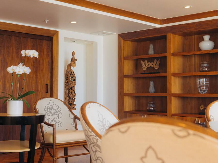 Een kamer met een houten boekenkast, een eettafel met stoelen en een kamerplant.
