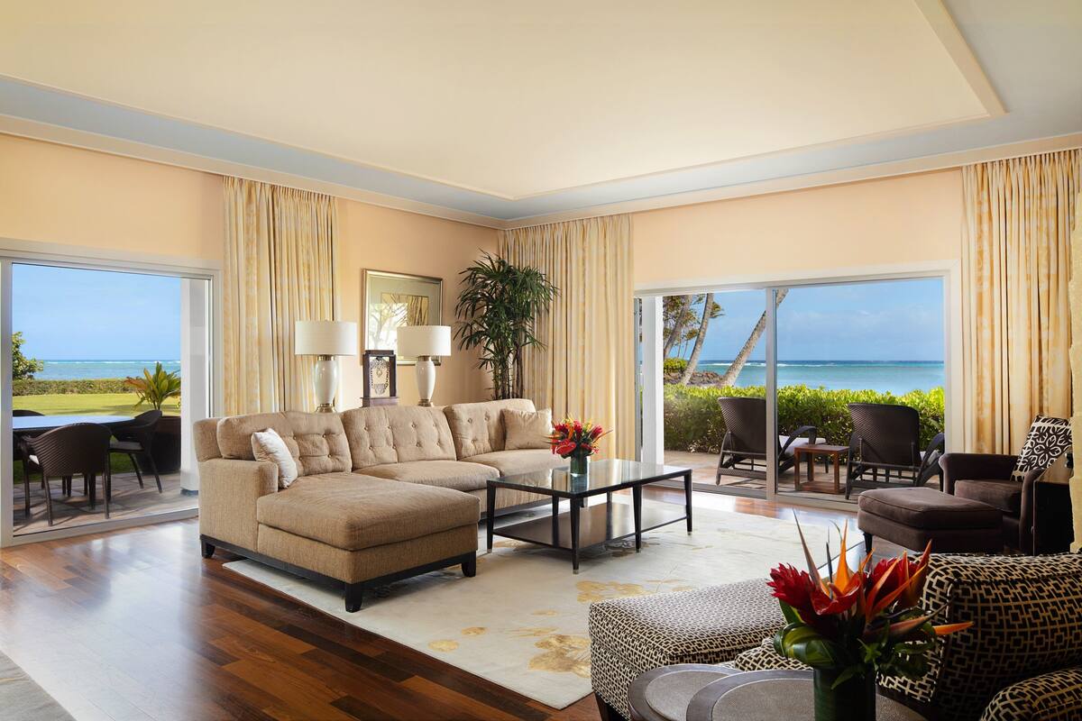 A spacious living room with a large beige sofa, a coffee table, and a view of the ocean.