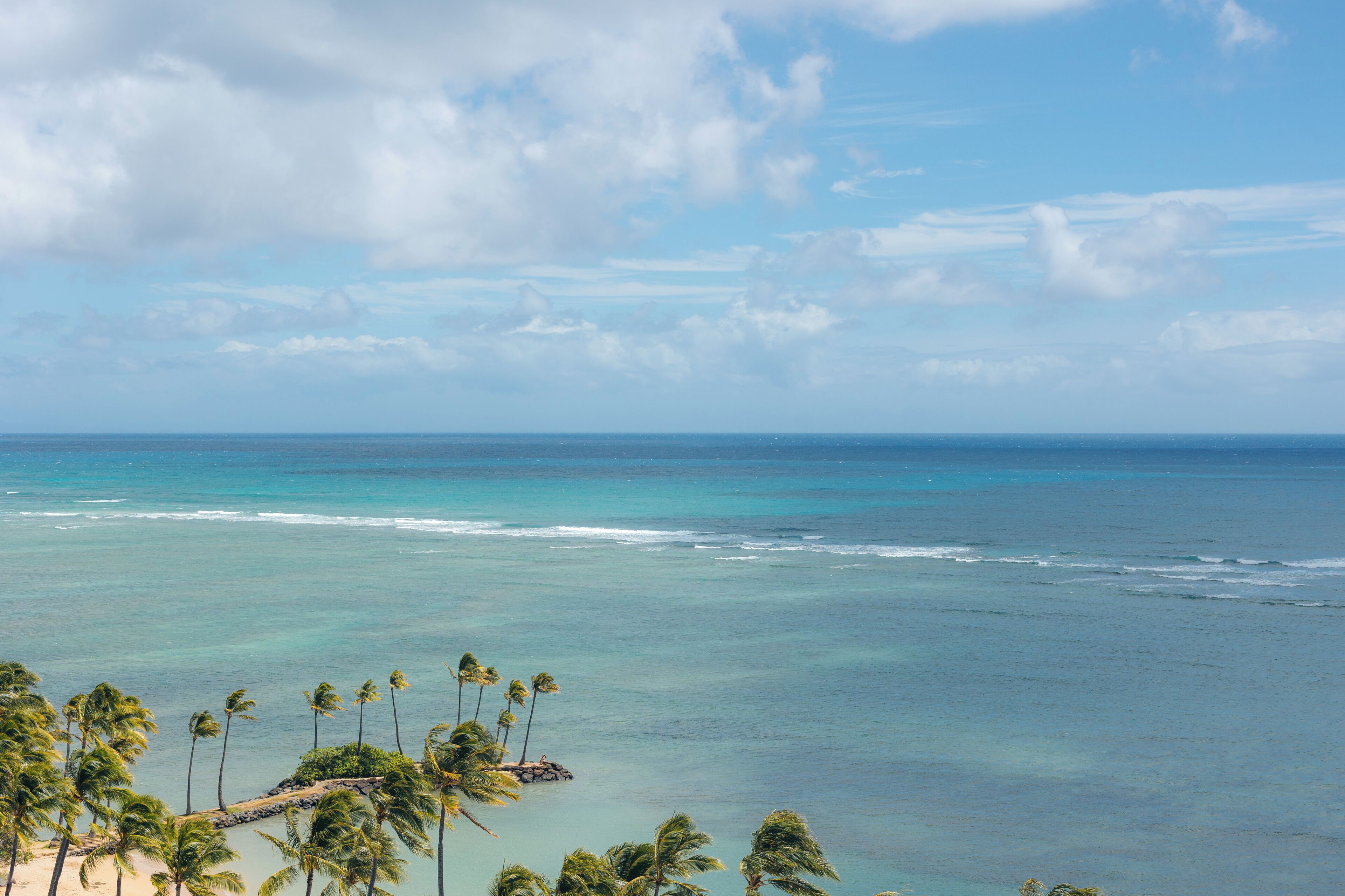 Une plage tropicale aux eaux d’un bleu limpide, bordée de palmiers et ponctuée d’un promontoire rocheux.