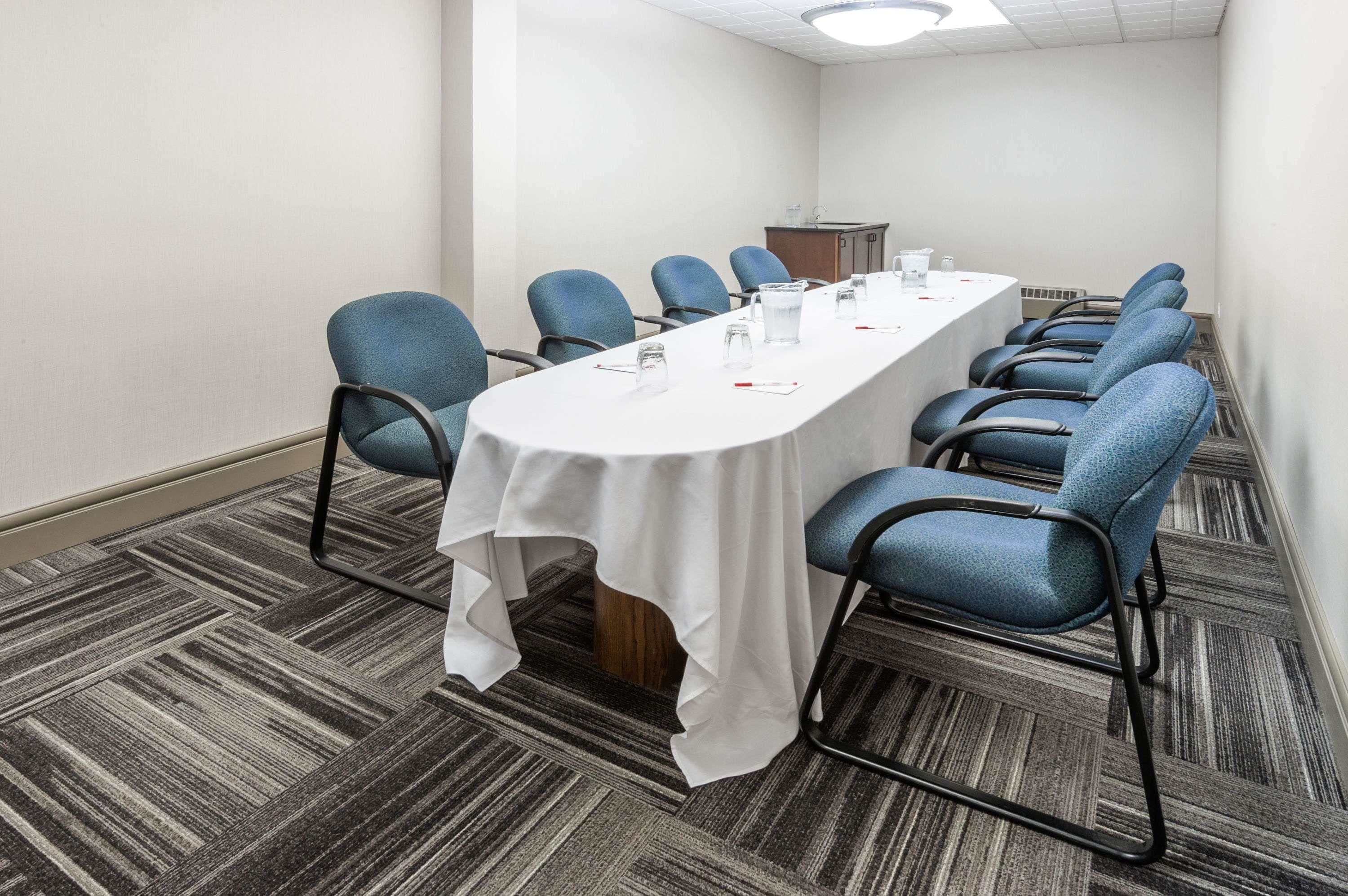 Uma sala de conferência com uma mesa comprida, cadeiras azuis e toalha de mesa branca.