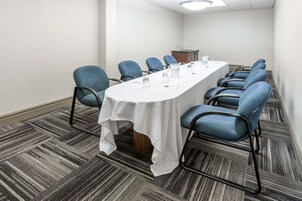 Un salón de conferencias con una larga mesa, sillas azules y un mantel blanco.