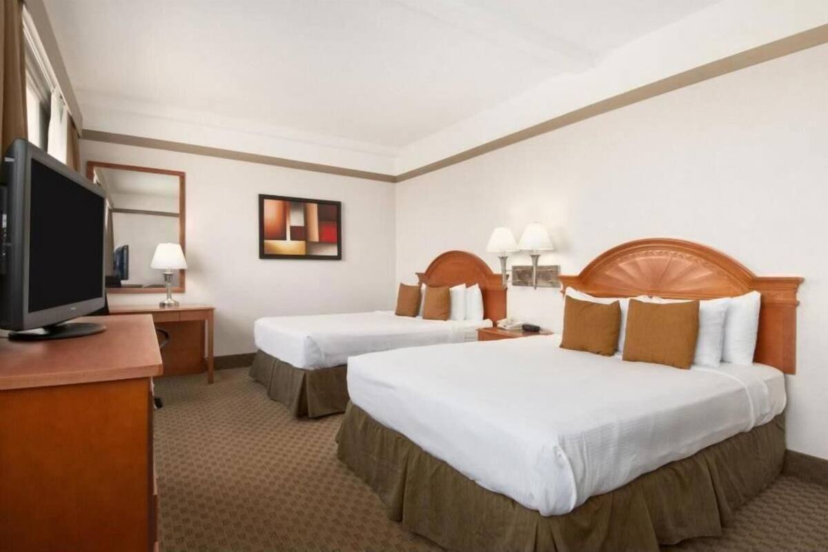 A hotel room with two beds, a desk with a television, a mirror, and a painting on the wall.
