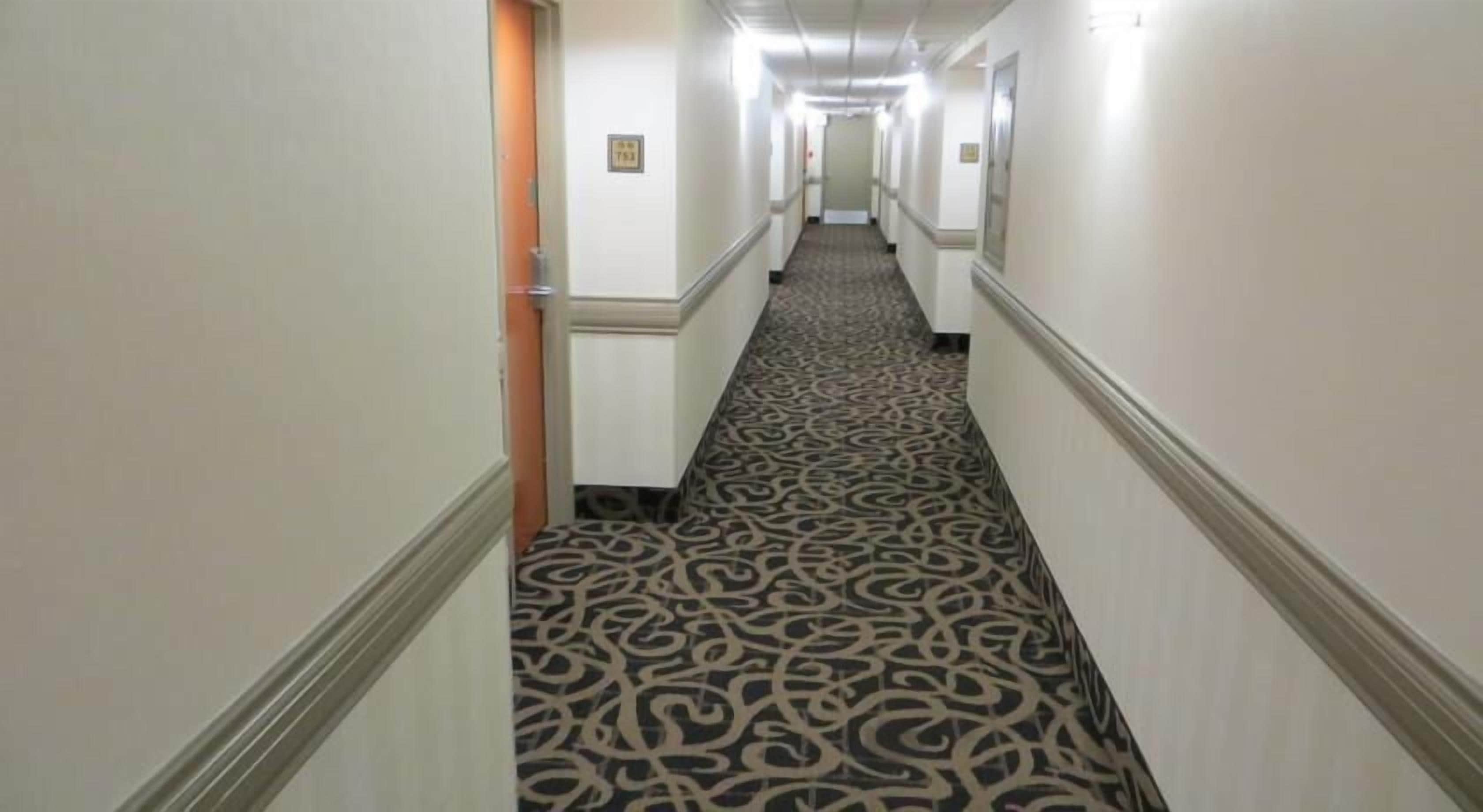 Pasillo de hotel con alfombra estampada, paredes blancas y puertas a ambos lados.