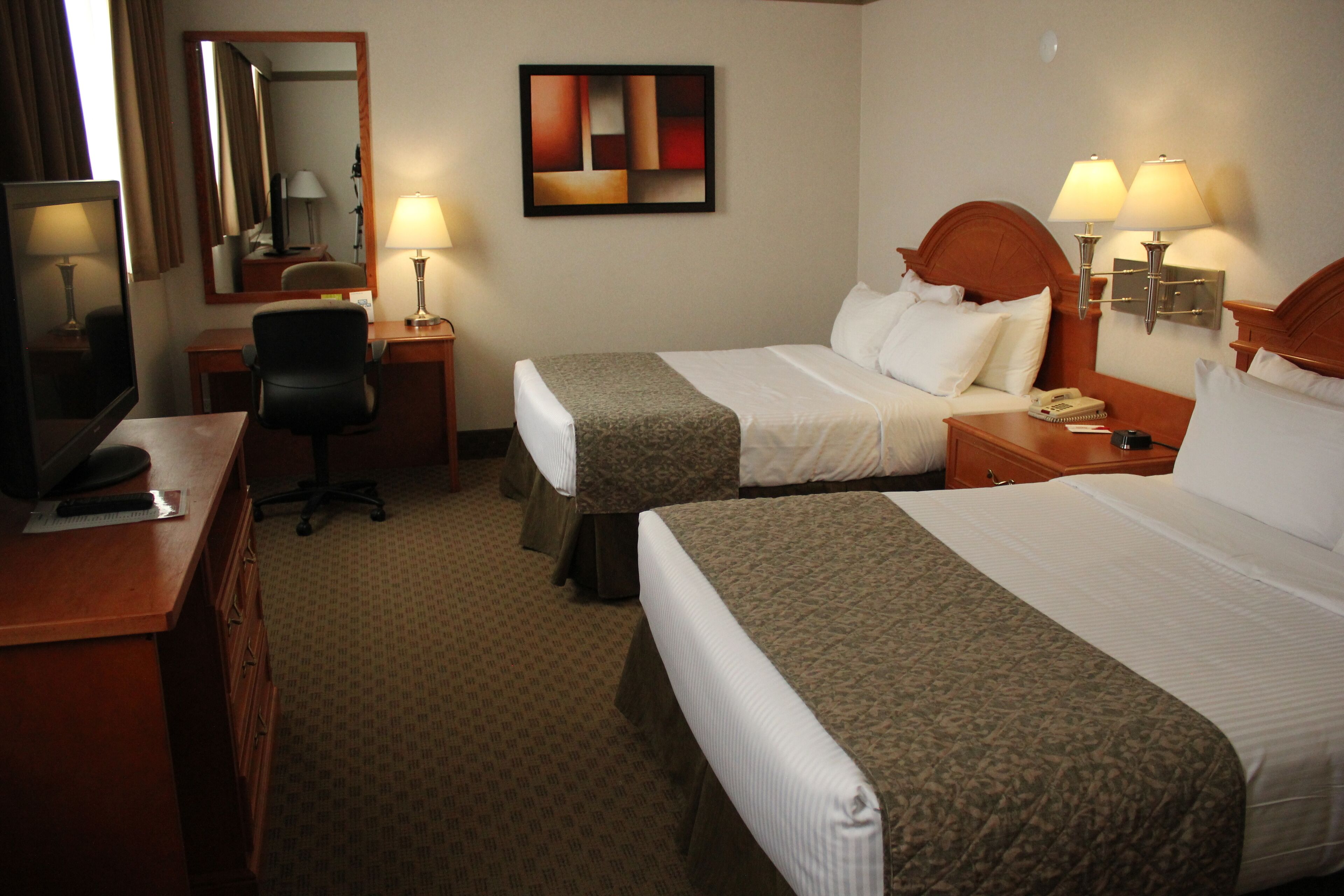 Une chambre d’hôtel avec deux lits, un bureau, une chaise, un miroir et deux lampes de chevet.