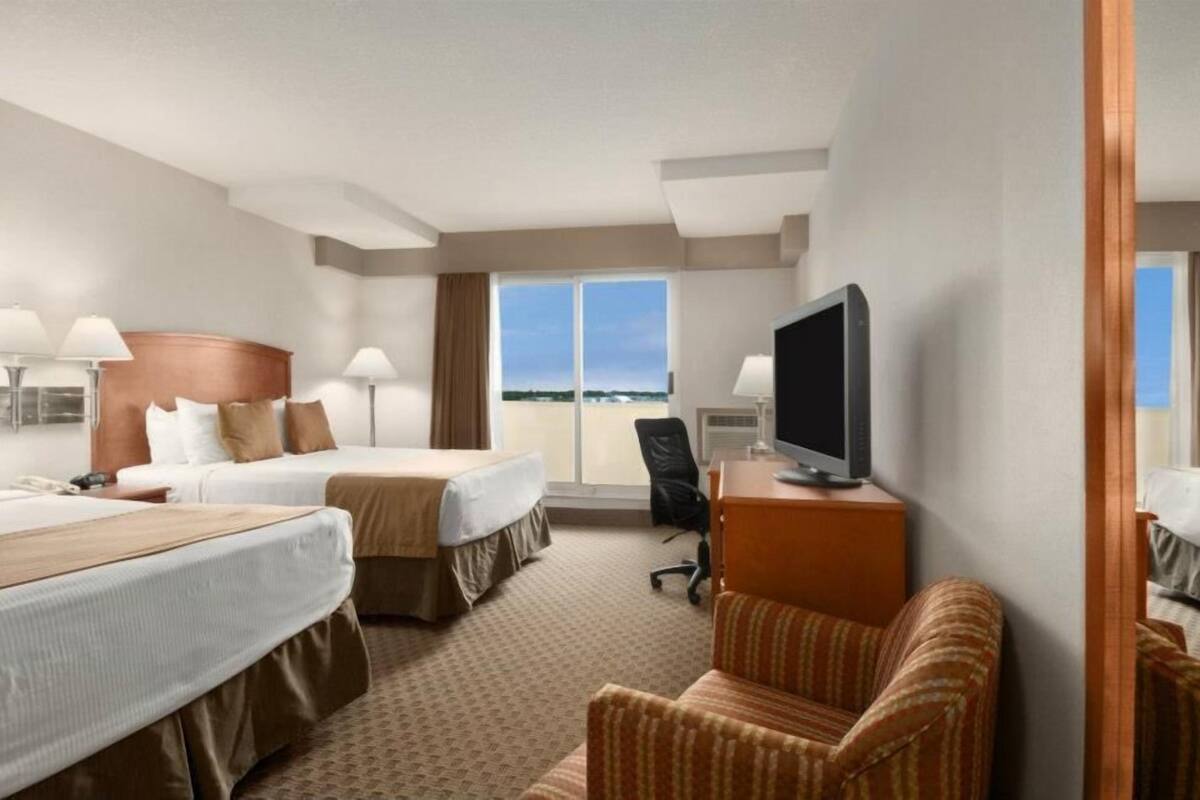 A hotel room with two beds, a TV, a desk, and a view of the ocean.