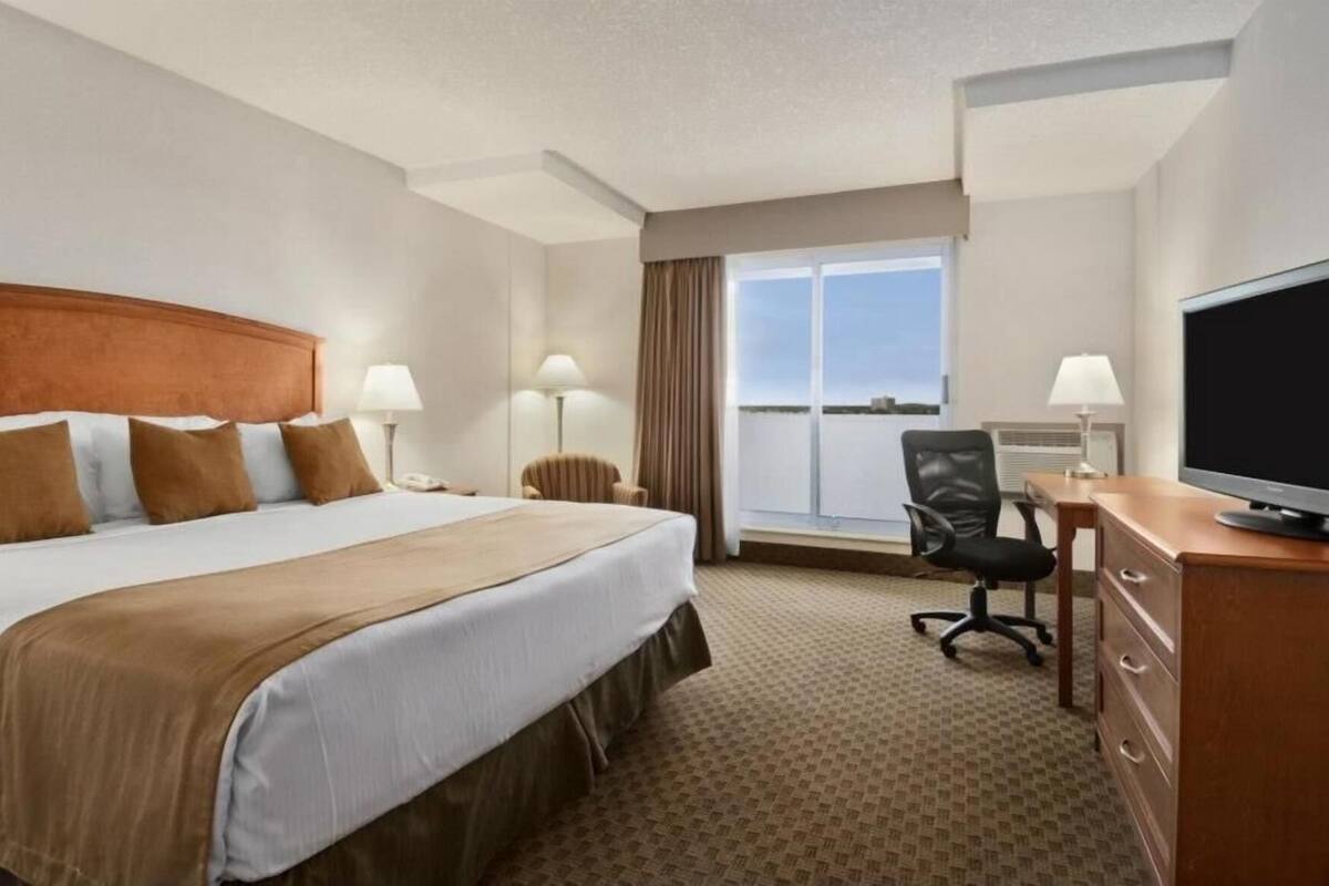 A hotel room with a bed, a desk, a chair, a television, and a window with a view.