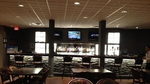 Een restaurant met een bar, tafels, stoelen en een televisiescherm.