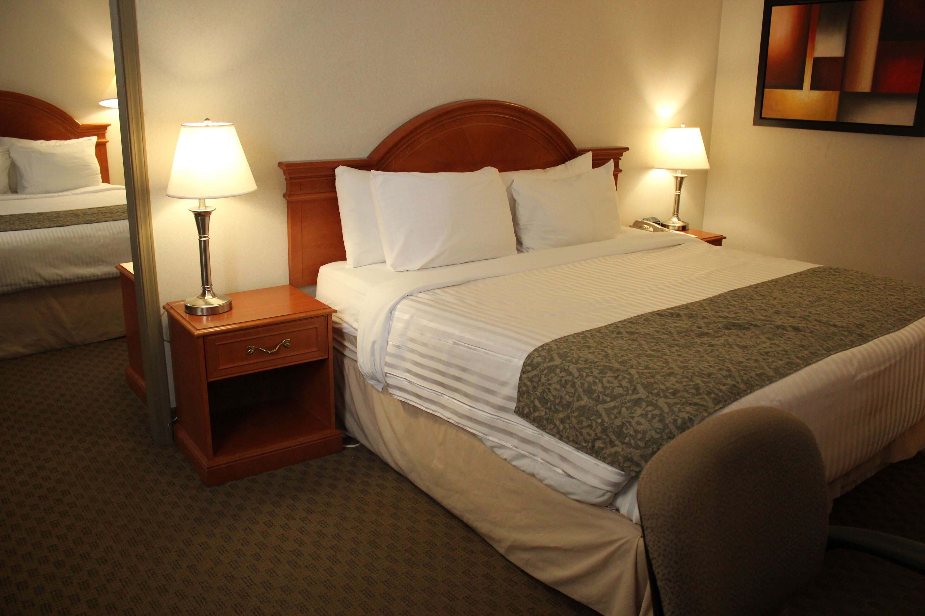 Habitación de hotel con una cama bien hecha, dos lámparas de noche, una mesita de noche de madera y un espejo en la pared.