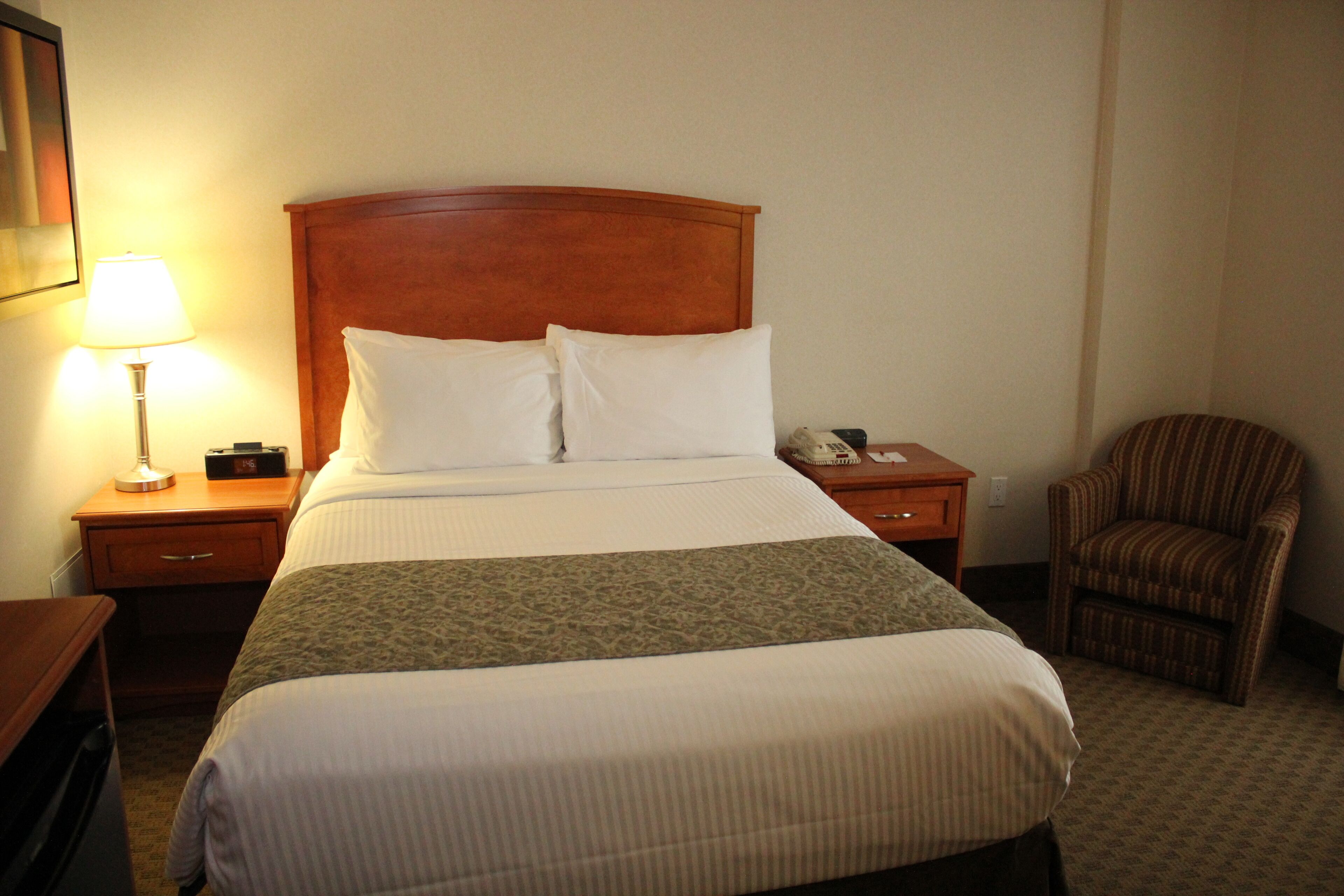 Een hotelkamer met een groot bed, een nachtkastje met een lamp, een stoel en een telefoon aan de muur.