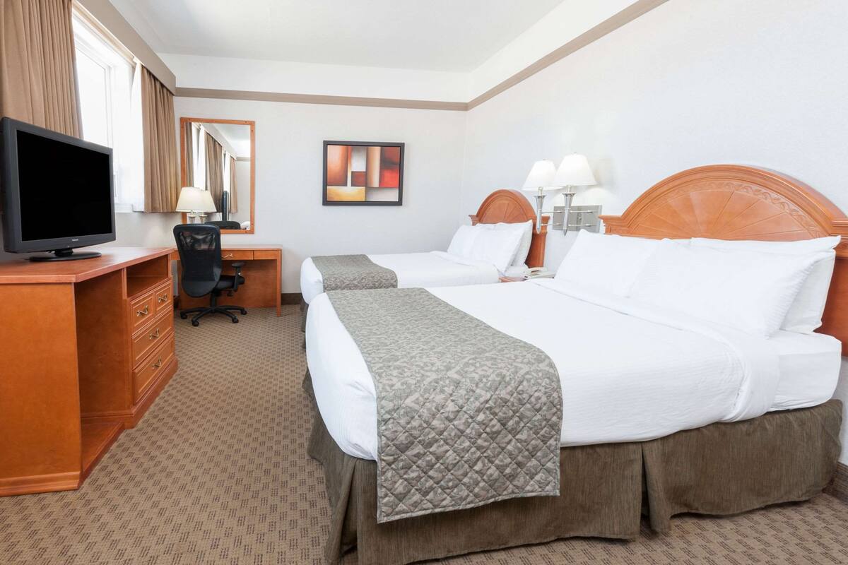 A hotel room with two beds, a desk with a computer, a chair, a television, and a mirror.