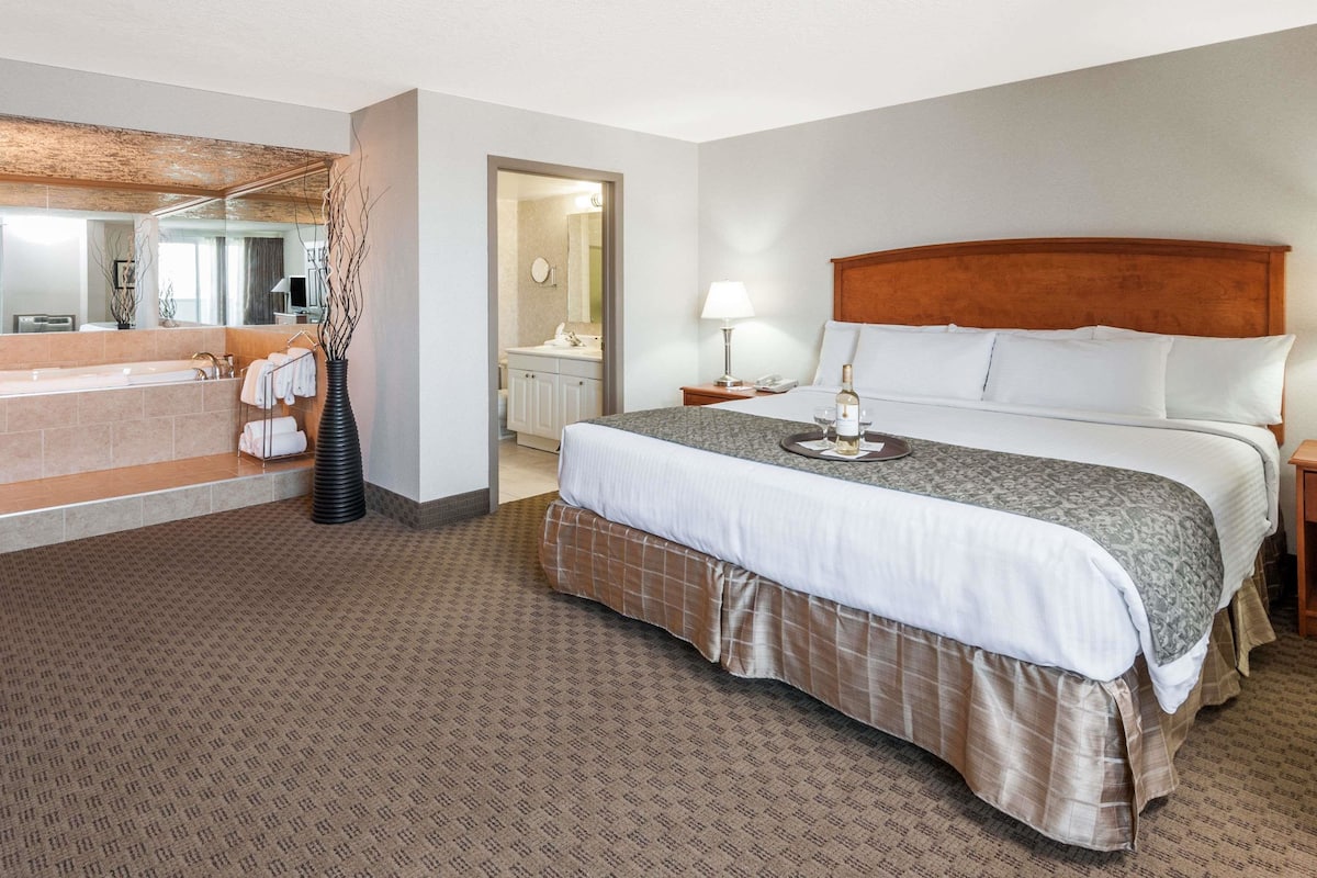 A hotel room with a large bed, a bathroom with a bathtub, and a mirror.