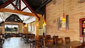 Een ruim restaurant met houten tafels en stoelen, een bakstenen muur en een groot raam met uitzicht op de omgeving.