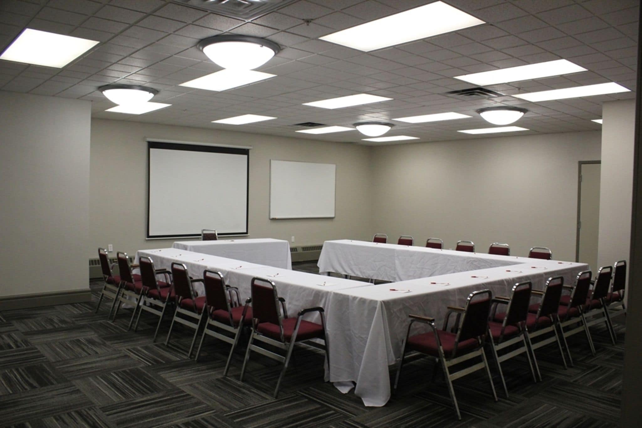 A conference room with a long table, red chairs, a white screen, and a projector.