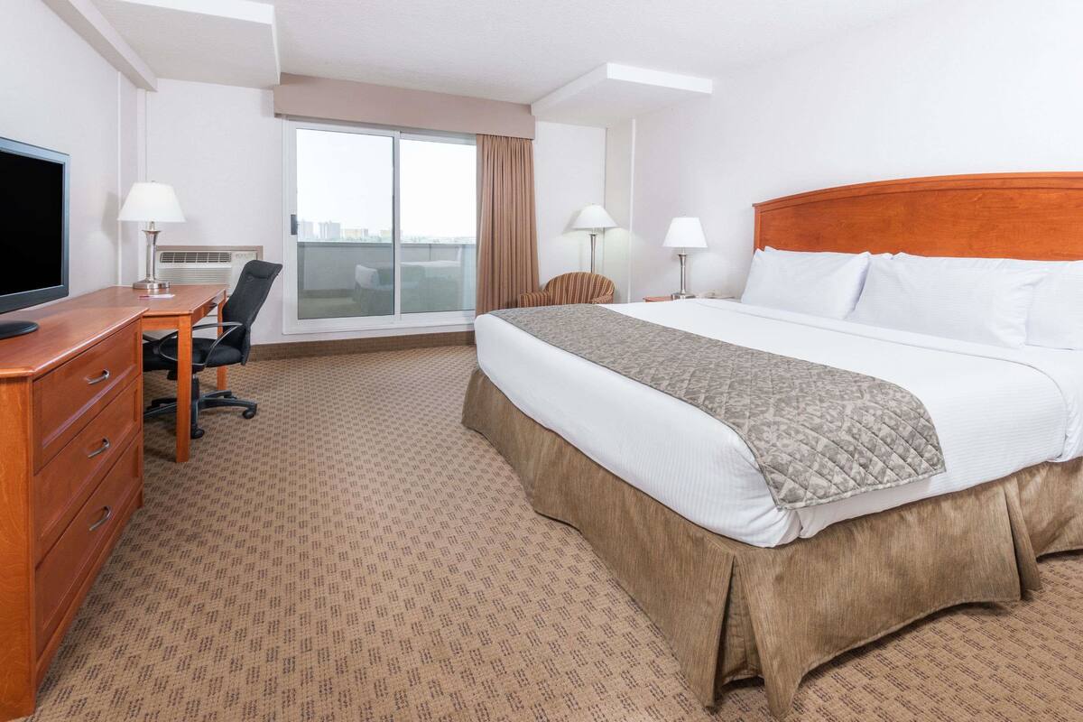 A hotel room with a large bed, a desk with a computer, a chair, and a TV.