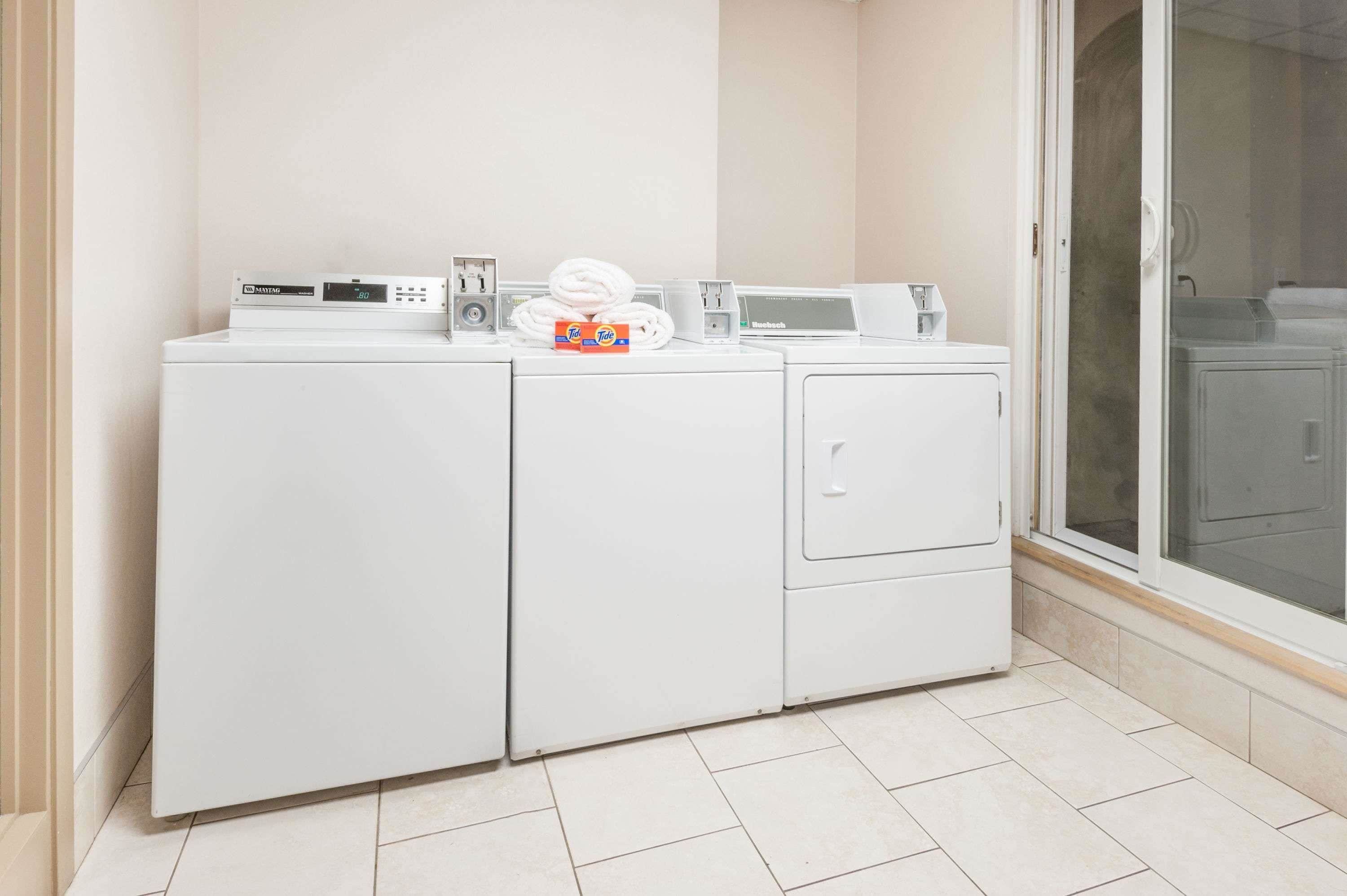 Un espace buanderie comprenant un lave-linge et un sèche-linge à chargement frontal, une pile de serviettes blanches et une boîte de lessive.