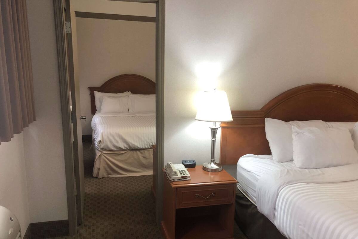 A hotel room with two beds, a bedside table with a lamp, a phone, and a small drawer.