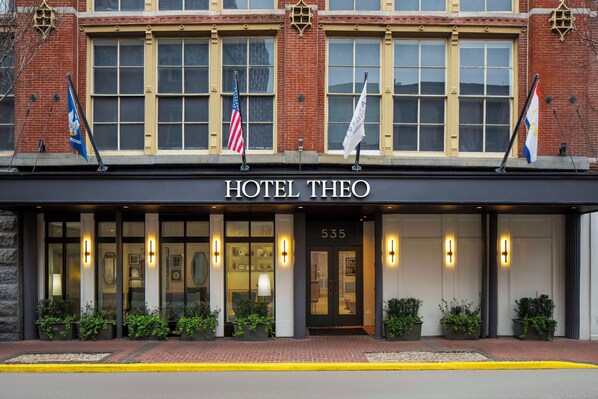 Welcome to Hotel Theo, featuring a classic brick facade with large windows and a prominent entrance.