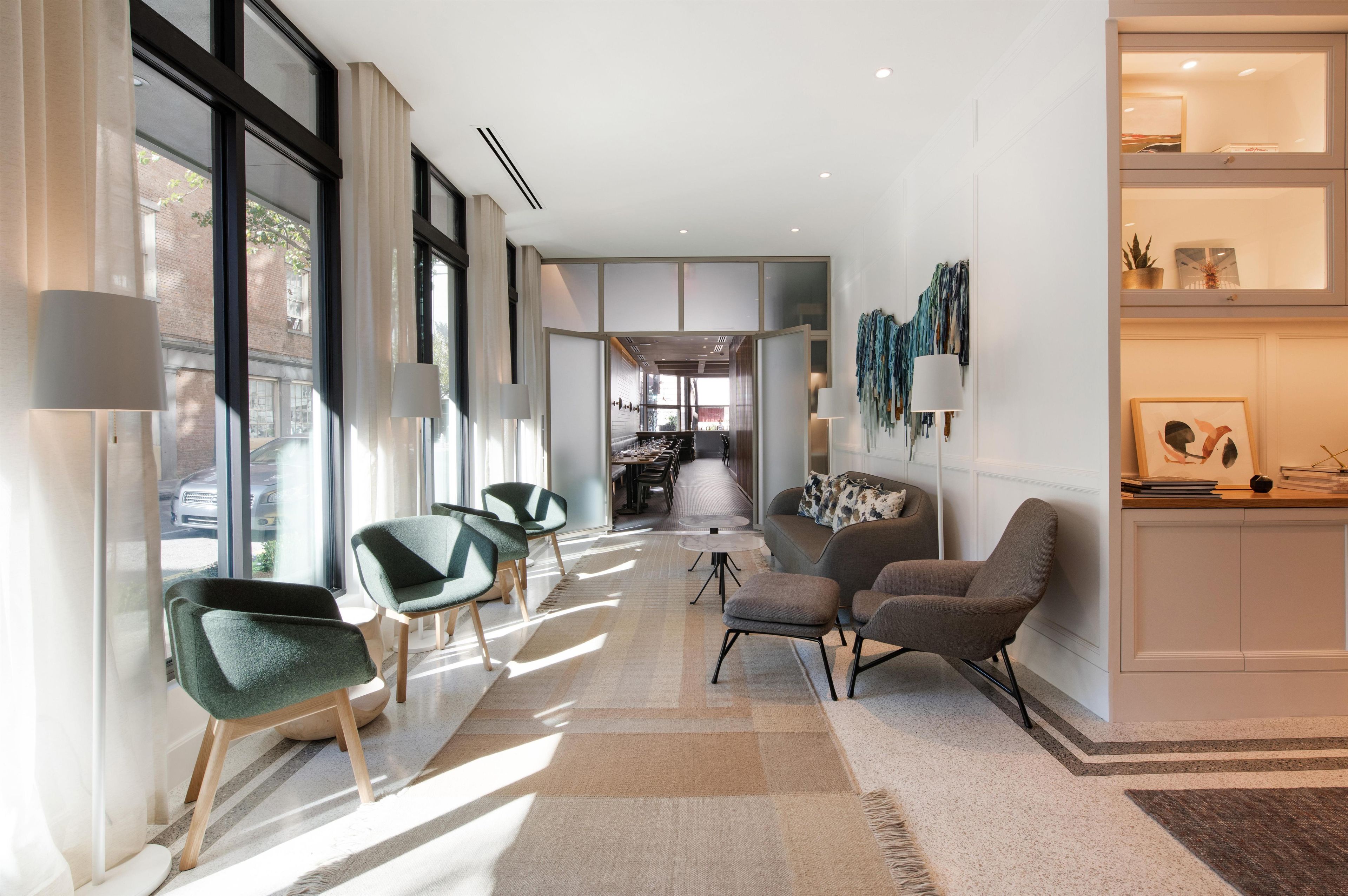 A modern living room with a sofa, chairs, and a coffee table. There is a dining area in the background with a long table and chairs.