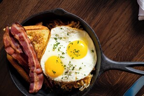 A skillet with two fried eggs, bacon, and toasted bread. - Hotel Theo New Orleans, Tapestry Collection by Hilton (New Orleans)