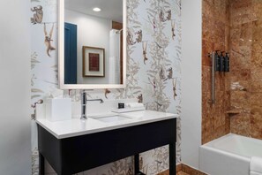 Bathroom features a patterned wallpaper, a bathtub with showerhead, and a large mirror above the vanity.