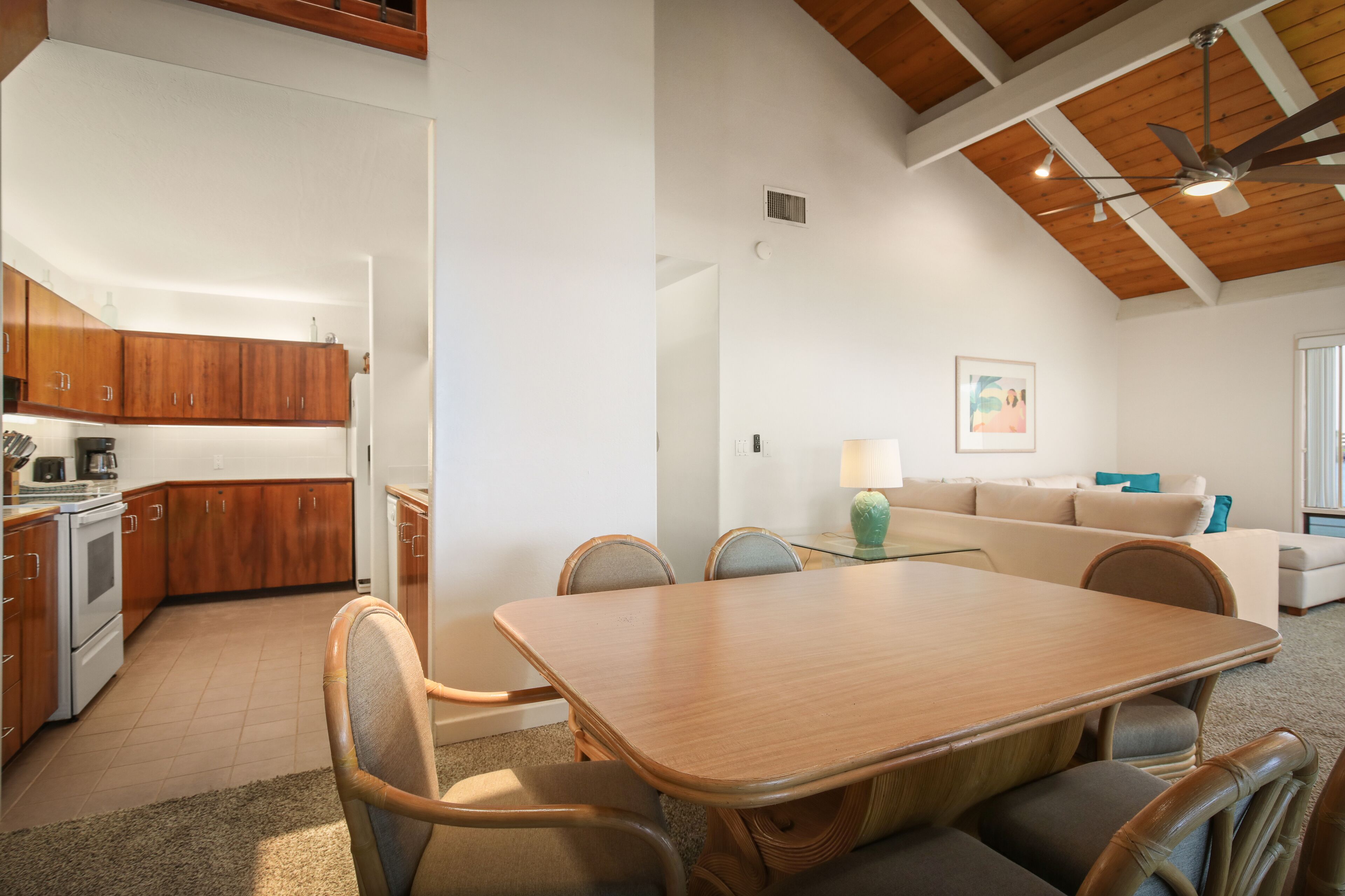 Una cocina amplia con armarios de madera, una mesa de comedor con sillas, un ventilador de techo y una sala de estar con un sofá y una lámpara.