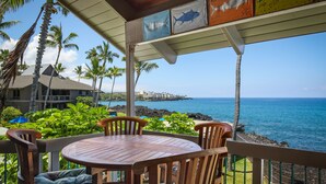 A wooden table and chairs on a balcony with a view of the ocean and a building in the background.
