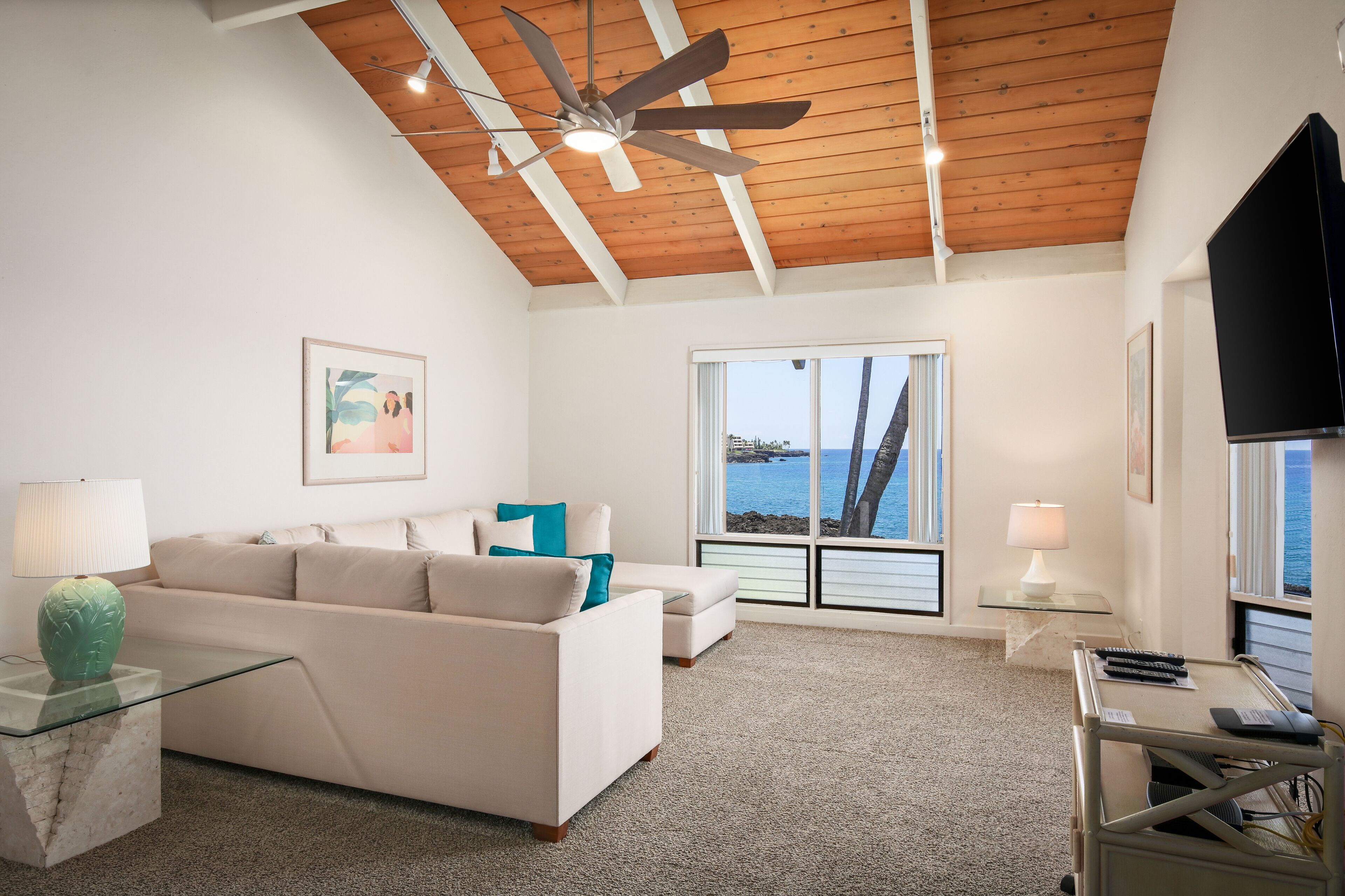 A living room with a ceiling fan, a sofa, a glass coffee table, a lamp, and a TV.