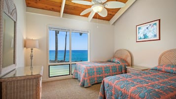 A bedroom with two beds, a ceiling fan, a large window with a view of the ocean, and a framed picture on the wall.