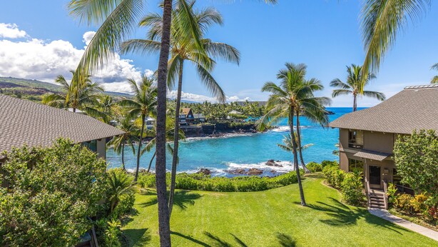 A resort with a view of the ocean, palm trees, and a well-maintained lawn.