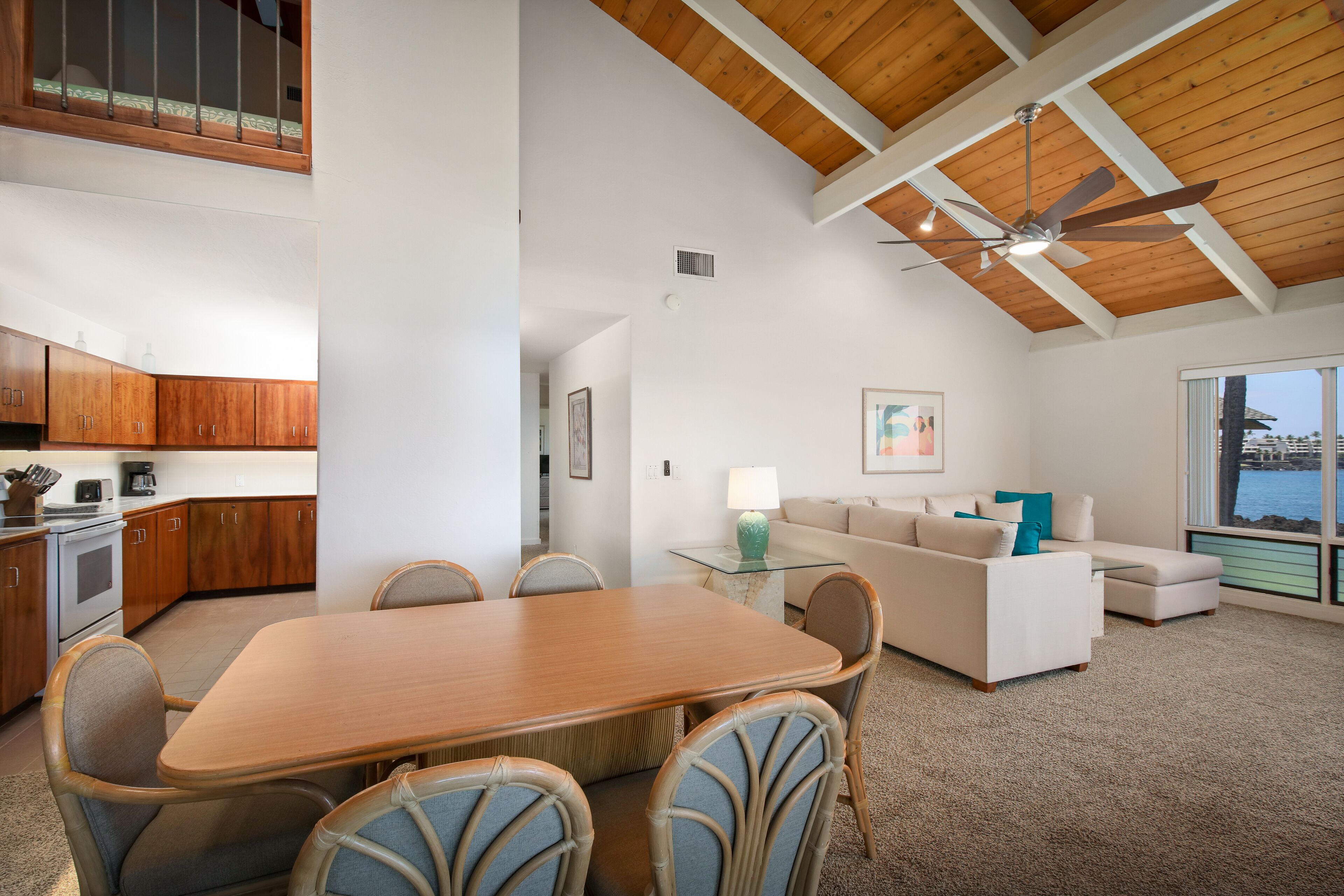 A spacious living area with a wooden ceiling, a dining table with chairs, a sofa, and a view of the outdoors.