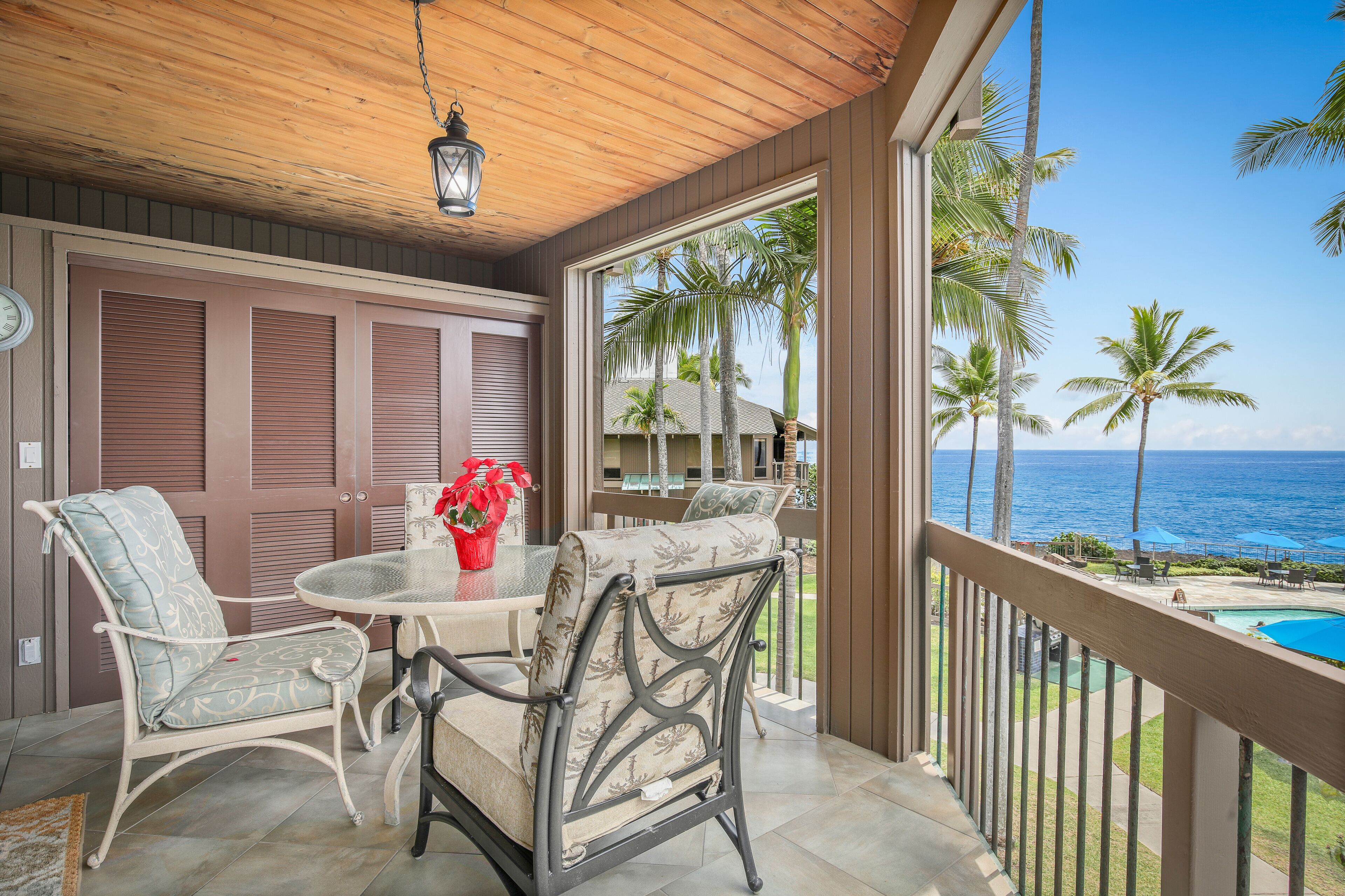 A covered outdoor seating area with two chairs and a table, overlooking a pool and palm trees.