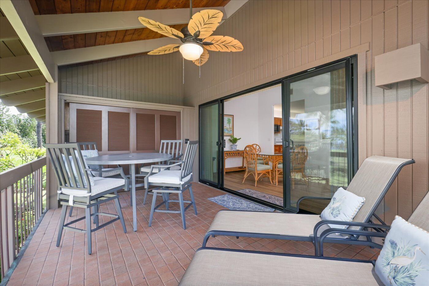 An outdoor patio with a dining table and chairs, a ceiling fan, and a sliding glass door leading to an indoor area with a kitchen and dining set.