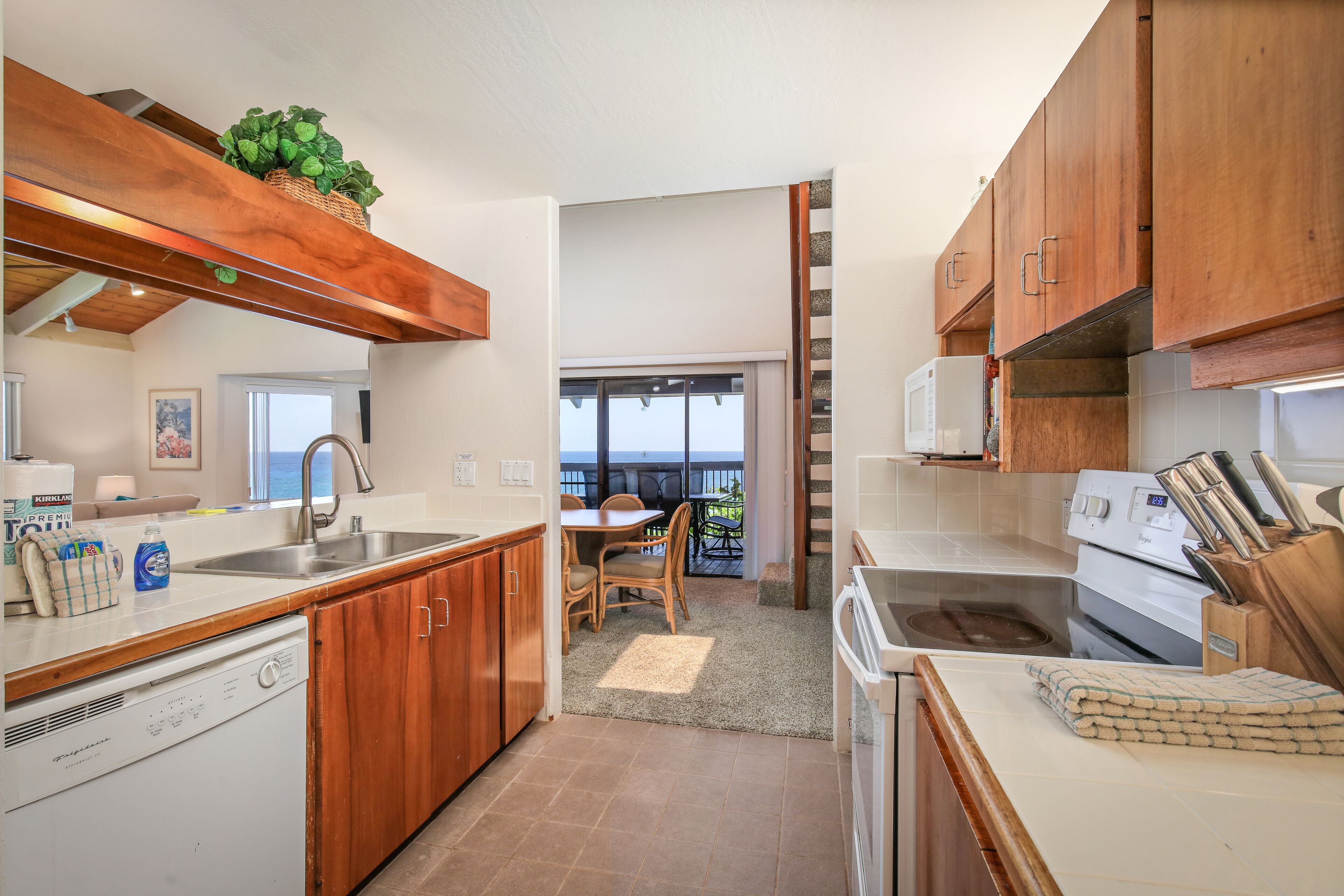 A kitchen with wooden cabinets, a dishwasher, a stove, and a dining area with a view to the outside.