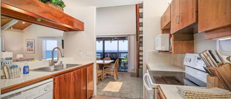 A kitchen with wooden cabinets, a dishwasher, a stove, and a dining area with a view to the outside.