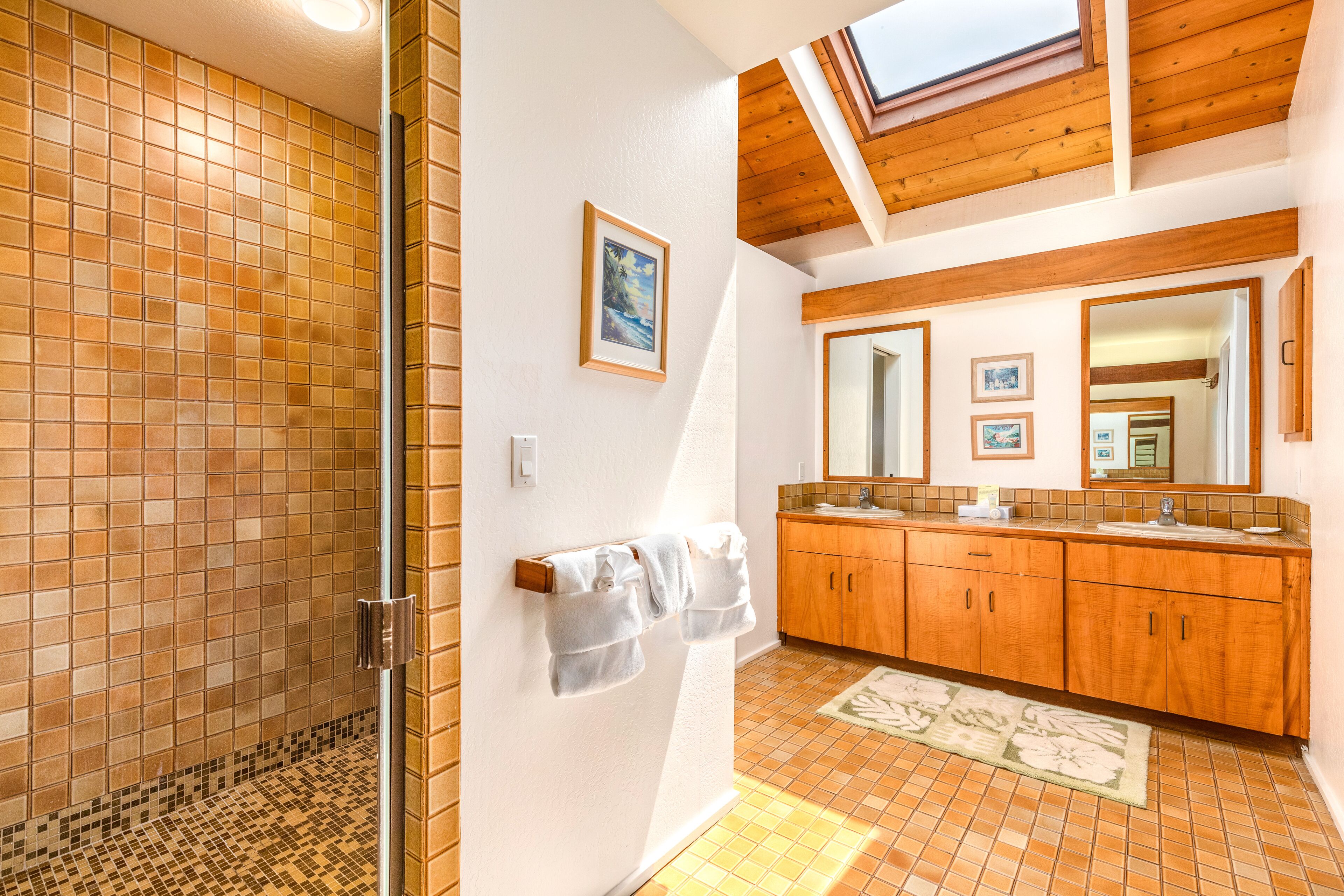 Un bagno con doccia, mobili in legno, un grande specchio e un lucernario.